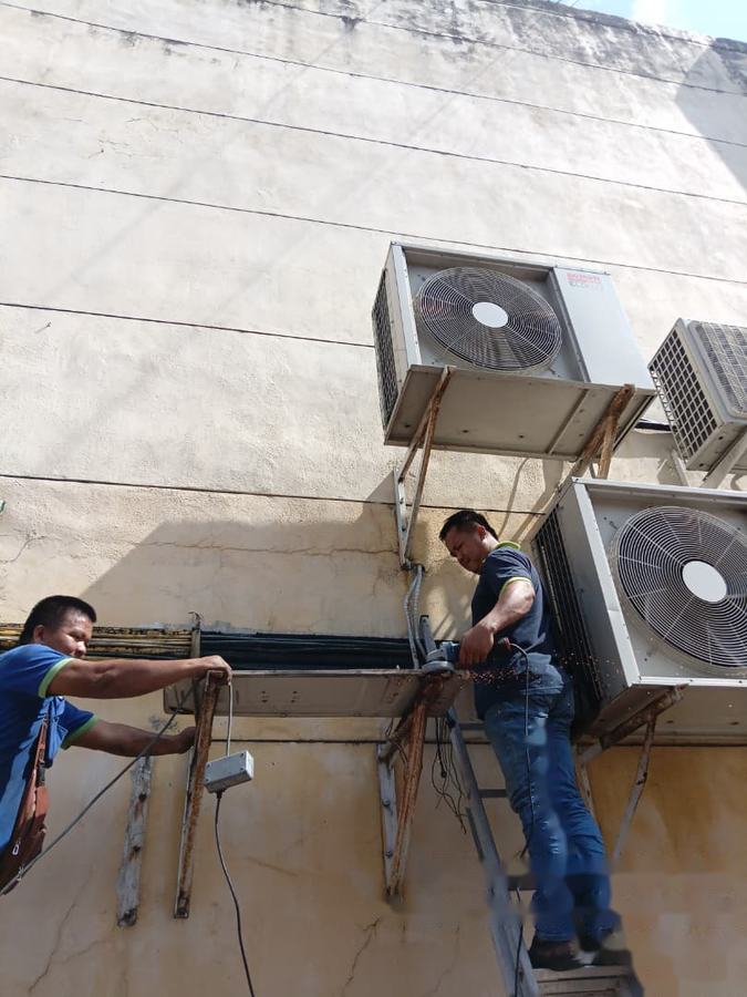 Technicians dismantling outdoor units on a building wall in Semporna